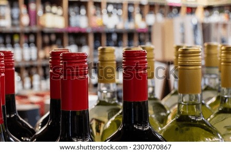 Red and golden caps of wine bottles close-up on blurred background of wine shelves Royalty-Free Stock Photo #2307070867