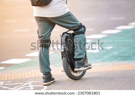 Man with knee pads on electric mono wheel waiting on crosswalk. Man on electric single wheel crossing street on crosswalk, rear view. Mobile portable individual transportation vehicle (EUC) Royalty-Free Stock Photo #2307081801
