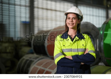 engineer woman standing with confidence with green working suite dress and safety helmet in front of warehouse of steel role material. smart industry worker operating.