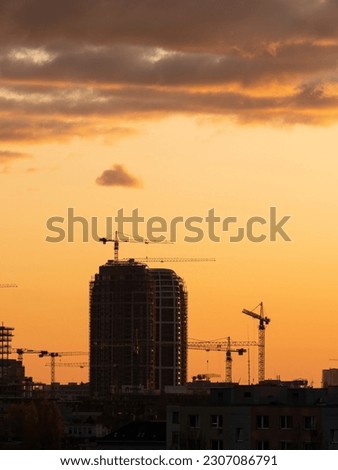 Silhouette of a skyscraper under construction process and cranes in the evening sky. New residential buildings being constructed.