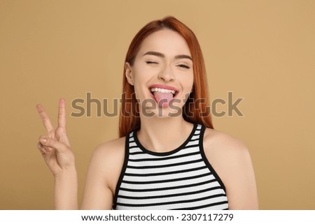 Happy woman showing her tongue and V-sign on beige background