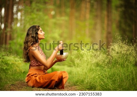Indian Woman playing Tibetan Singing Bowls with Mallet Outdoors. Relaxing Meditative Music Therapy and Sound Healing. Spiritual Yoga Meditation Practice in Forest Royalty-Free Stock Photo #2307155383