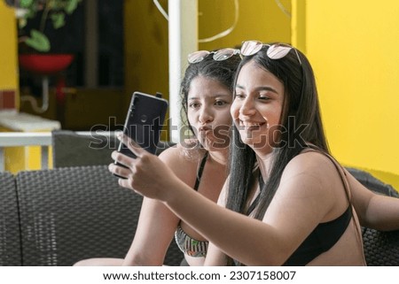 two beautiful latin women are taking a photo with their cell phone, laughing and making gestures with their mouths