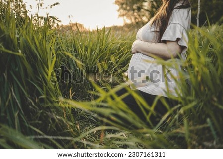 Close-up of pregnant woman with hands on her belly on nature background. Concept of pregnancy, maternity, expectation for baby birth.