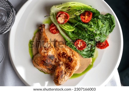 Half of a roasted chicken, on plate with herbs and tomatoes.