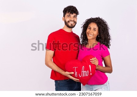 Young loving couple holding a heart pillow written in Portuguese ''I love you''. Valentines day 
