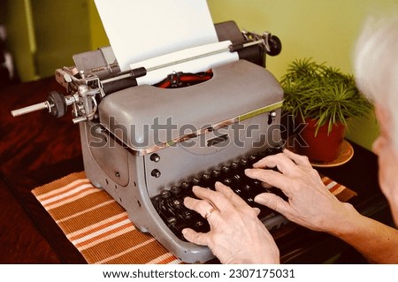 Grandma writes with an old gray typewriter. The picture is vintage style  70s with light green wall. Typewriter and green plant is on the brown table.