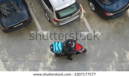 Delivery service. driver man in helmet with blue thermo backpack sitting on a moped . top view. courier waiting for customer near house.  male on scooter.  Royalty-Free Stock Photo #2307177577