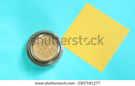 South Indian homemade filter coffee cup and yellow paper on blue background, top view