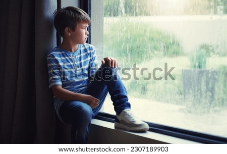 Little boy, home and watching the rain by window of natural water drops and thinking in relax indoors. Child relaxing by windowsill looking out glass at storm in lonely or sad for weather at house Royalty-Free Stock Photo #2307189903