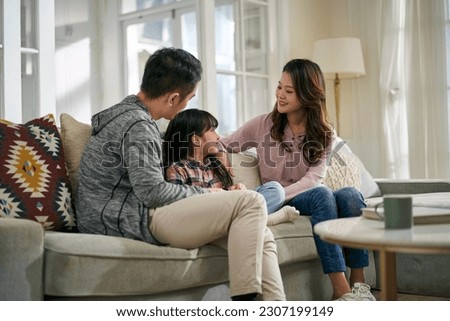 young asian mother and father sitting on family couch at home having a pleasant conversation with daughter Royalty-Free Stock Photo #2307199149