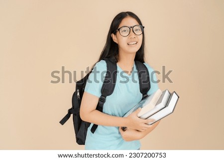 A happy Asian female student wears glasses and carries a book