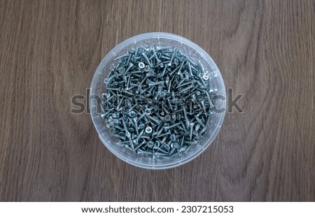Round plastic jar with chrome-plated metal screws.Sale of small screws for fixing the material.
