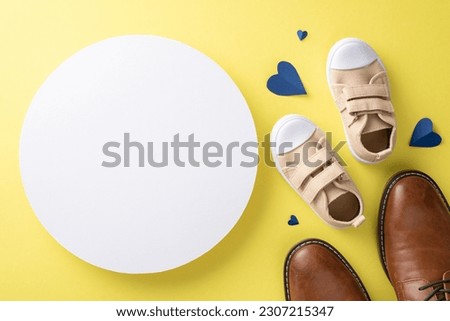 Father's Day greetings from son and dad. Top view of leather shoes, baby sneakers, and hearts on yellow background with circle for message or logo