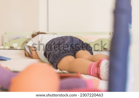 Caucasian toddler falling asleep in bed after having been playing. Rest time, relax.