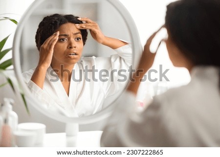Skin Aging. Shocked Black Woman Looking In Mirror At Her Wrinkles On Forehead, Millennial African American Female Examining Fine Lines On Face, Selective Focus On Reflection, Closeup