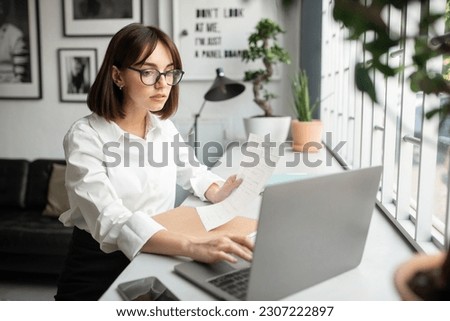 Successful entrepreneurship career. Glad lady sitting at table with laptop, reading document in cafe or cozy office interior. Modern business and work, startup planning