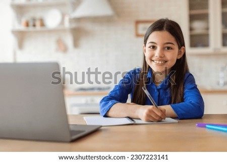 Online Education. Happy Young Girl Taking Notes At Laptop Embracing E-Learning, Studying From Home, Sitting At Desk Doing School Homework. Shot Of Successful Schoolgirl During Digital Class