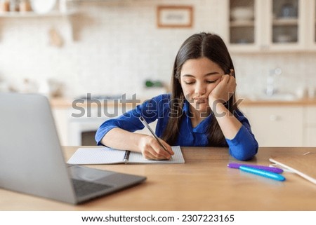 Online Education Burnout. Unhappy Schoolgirl Taking Notes At Laptop Tired Of Difficult Homework Sitting At Table At Home. Depressed School Kid Engaging In E-Learning. Problems Of Distance Classes