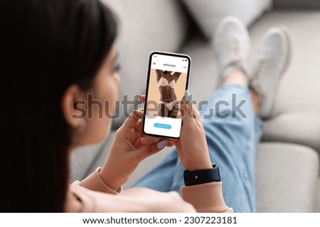 Young arab woman use phone for online shopping, choose underwear in fashion store on screen, rest on sofa at home. Order delivery, sale for shopaholic, app and website for new clothes