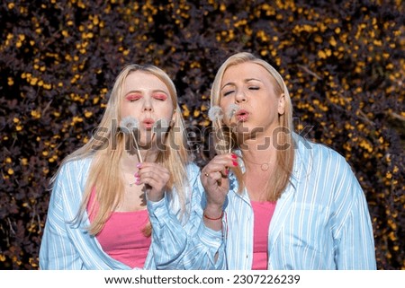  Mother and daughter look similar and blowing white dandelions. Relatives have fun together outside, enjoying nature. Mom and baby hike in park. Relatives interact with each other. Royalty-Free Stock Photo #2307226239