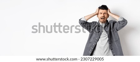Frustrated guy crying and panicking, holding hands on head and screaming distressed, having trouble, standing upset on white background. Royalty-Free Stock Photo #2307229005