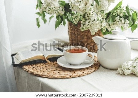 A cup of tea, a basket of lilacs and an open Bible.