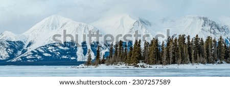 Stunning landscape views from the small town of Atlin in British Columbia during winter season with snow capped mountains in panoramic view. Huge frozen lake with spectacular arctic scenery. Royalty-Free Stock Photo #2307257589