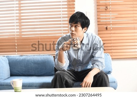 Relaxed young asian man having a drink indoors
