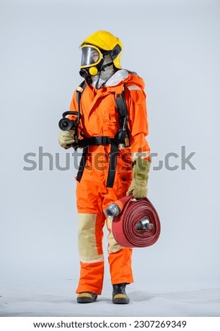 Vertical picture of a firefighter wearing a yellow helmet is standing while holding a fire hose.