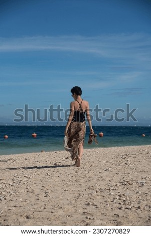 Rear view of young attractive girl dancing turning around by sea beach in summer vacation. Stylish pretty woman with short black hair wears in leopard pant having fun on the beach with copy space.