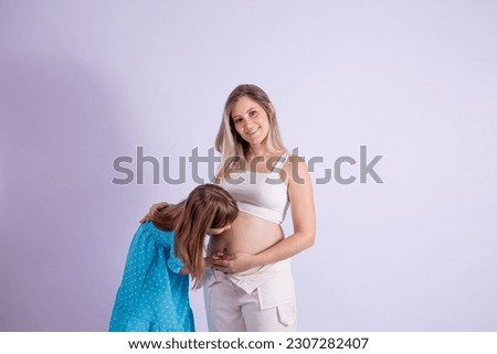 little daughter kisses her pregnant mom's belly. Happy older sister kissing mommy's belly expecting baby