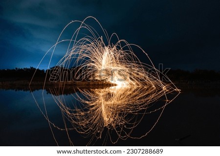 Beautiful figures and flashes of light painting reflected in a lake at night.
