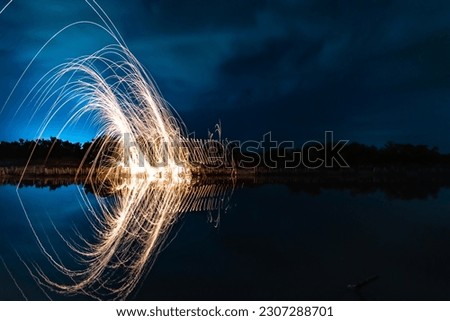 Beautiful figures and flashes of light painting reflected in a lake at night.