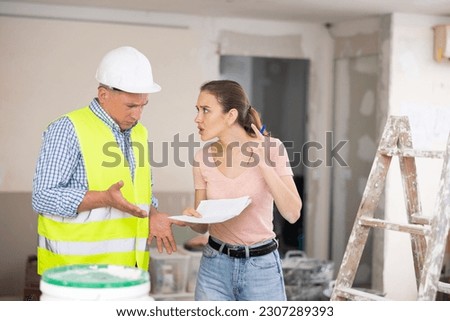 Man engineer and woman designer disputing about signing contract in apartment during repair works. Royalty-Free Stock Photo #2307289393