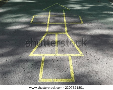 Painted yellow lines contrast against the dark asphalt and form the classic school playground game of Hopscotch