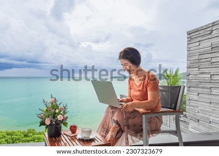 Senior digital nomad woman working at luxury villa in Phuket. andaman sea as background.