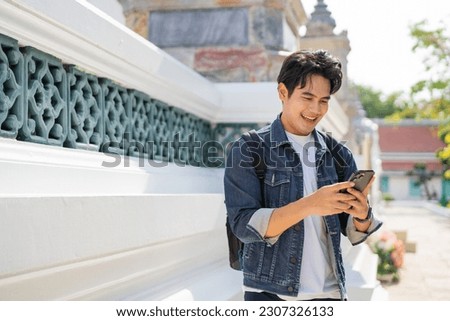 Portrait of Asian male traveler using a mobile phone on sidewalk of buddhist temple on street in Bangkok, Thailand, Southeast Asia - smart phone and internet for traveling concept Royalty-Free Stock Photo #2307326133