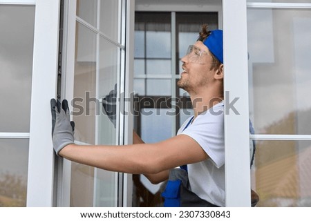 Qualified window repair specialist checks the fittings on the plastic window. Window maintenance wizard keeps the white window sash open with his gloved hand Royalty-Free Stock Photo #2307330843