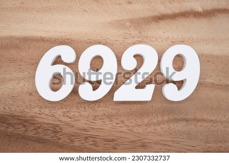 White number 6929 on a brown and light brown wooden background.
