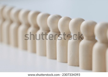 Small wooden figures lined up in long row on white table. Discipline and strict control of employees at work in office. White figurines made of wood Royalty-Free Stock Photo #2307334393