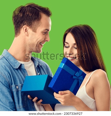 Love, dating, celebrating, lovers concept - happy smiling amorous couple opening gift box. Isolated on green color background. Square photo.
