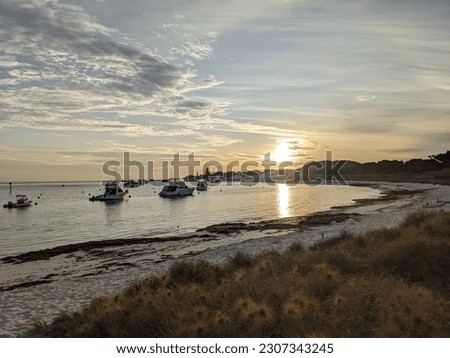An energetic sunset happening over a lazy scene. Moored boats of holiday makers stay and bask under the sky. Night sky with contrasting, powerful clouds sit motionless above. The sea is gentle. 