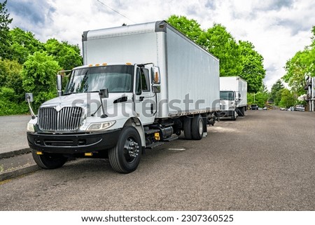 Industrial middle duty day powerful cab compact white rig semi truck with chrome parts and big box trailer standing on the urban city street making the local delivery for different business needs Royalty-Free Stock Photo #2307360525