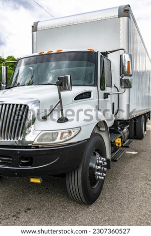 Industrial middle duty day cab white rig semi truck with chrome parts and big box trailer standing on the city street waiting for the next load for local delivery for different business needs