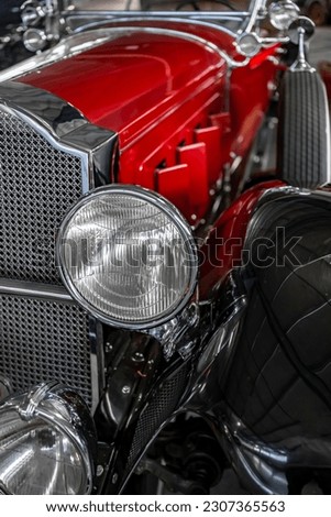Fragment of a shiny red and black retro car with unique design of an elegant shape of the chrome grille on this vintage car and with round headlights and opening air-cooling flaps