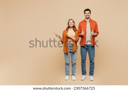 Full body young couple two friends family man woman wear casual clothes together point index finger aside on workspace area mock up show thumb up isolated on pastel plain beige color background studio
