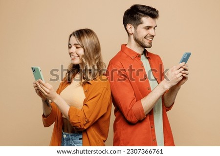 Side view young couple two friends family man woman wear casual clothes hold in hand use mobile cell phone together stand back to back isolated on pastel plain light beige background studio portrait
