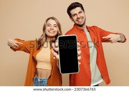 Young couple two friends family man woman wears casual clothes hold in hand use point finger on mobile cell phone with blank screen workspace area together isolated on pastel plain beige background