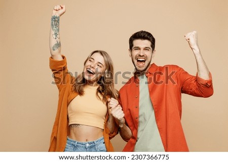 Young couple two friends family man woman wear casual clothes looking camera together do winner gesture celebrate clenching fists say yes isolated on pastel plain light beige color background studio Royalty-Free Stock Photo #2307366775